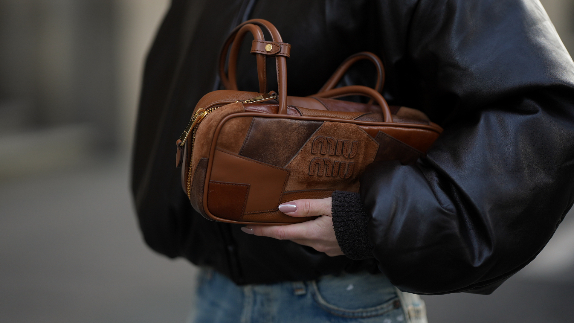 Nail Trends Romina Meier is seen wearing a dark brown bomber jacket with a coated leather finish, zip closure and classic collar from Acne Studios; distressed and painted wide-leg light-wash denim jeans from Acne Studios; a cognac brown Miu Miu Beau Patchwork leather handbag with patchwork pattern in different shades of brown from Miu Miu on November 10, 2025 in Duesseldorf, Germany