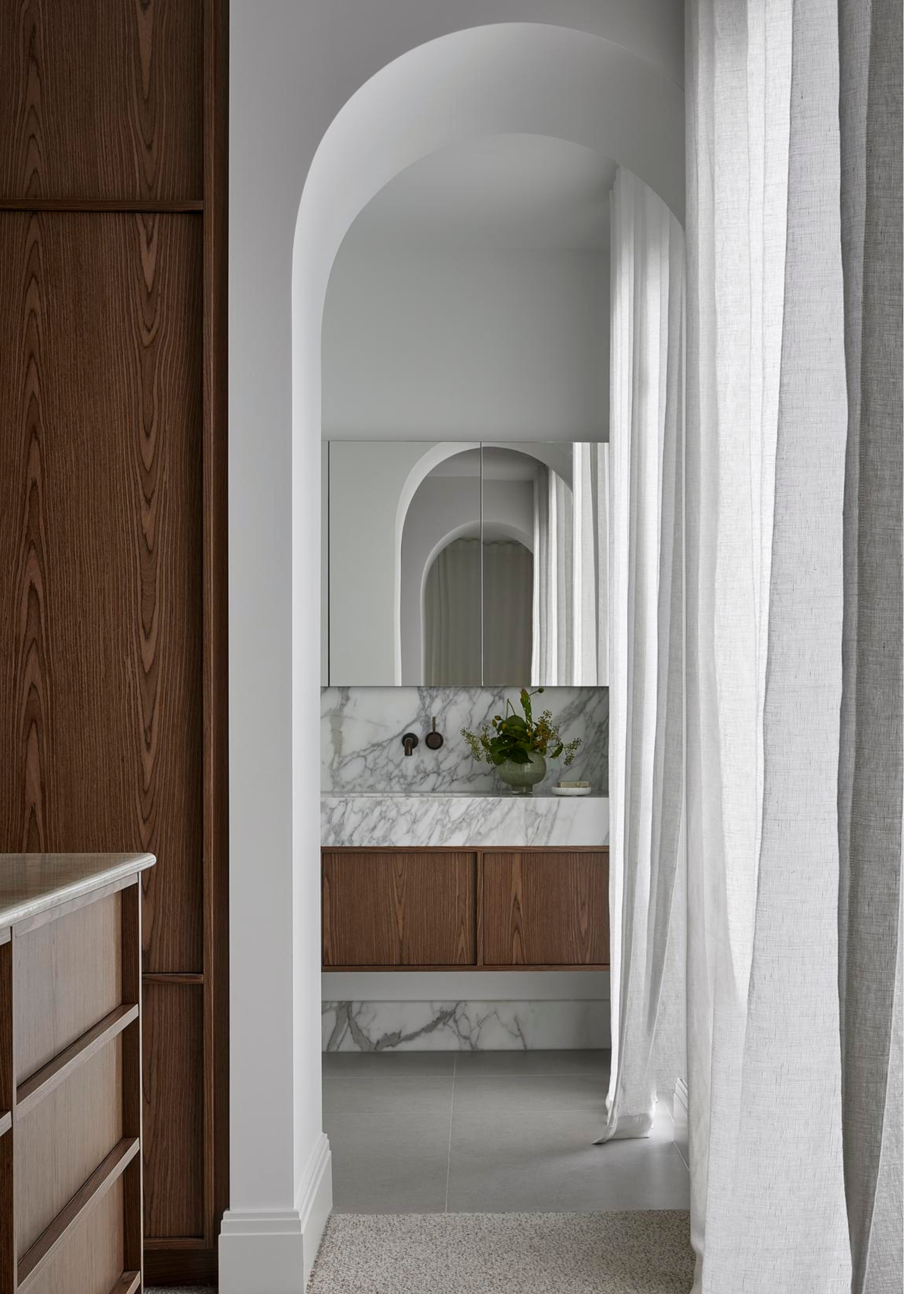 an airy en suite through an arched doorway with marble counters and wooden cabinets