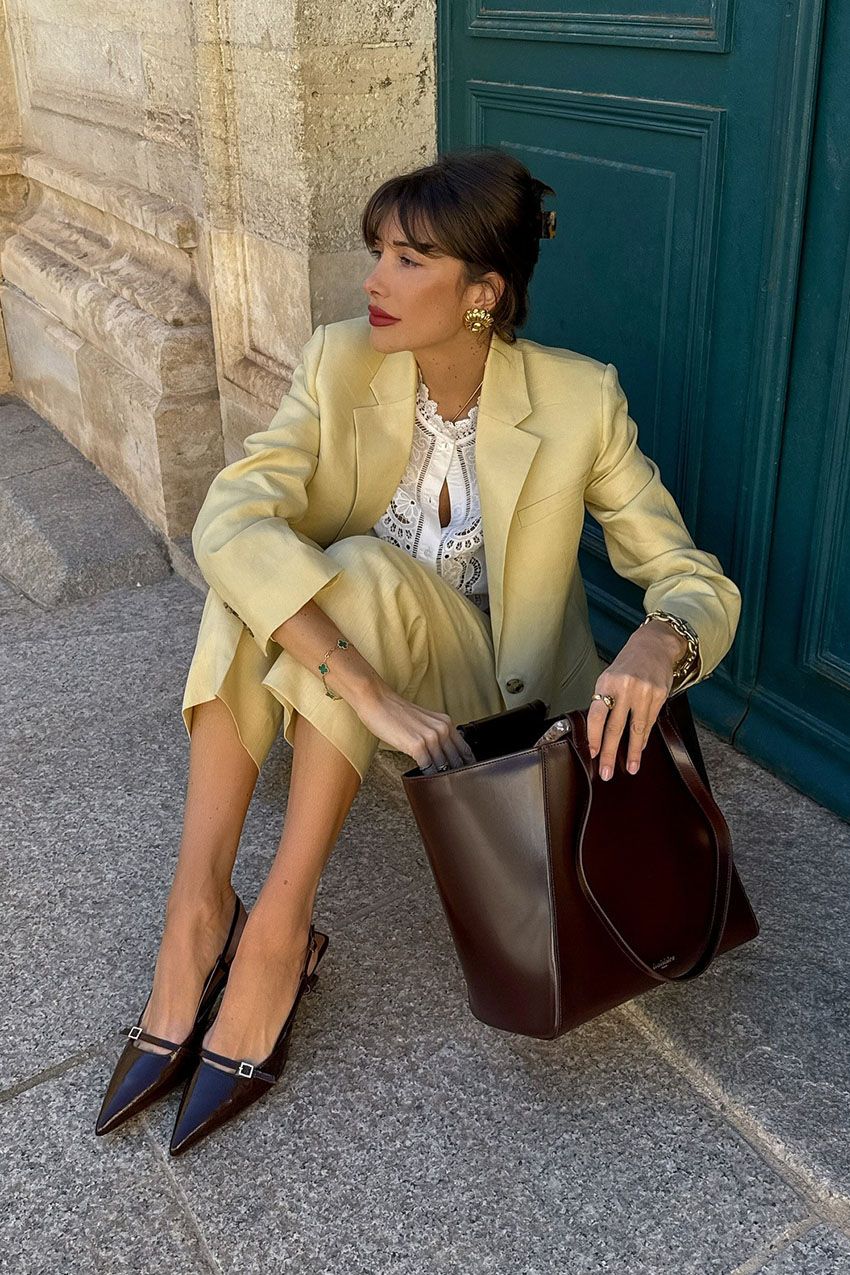 A French woman wearing a yellow suit, a brown leather bag, and brown pointed-toe slingback heels
