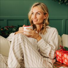 A beautiful blonde woman is sitting on the sofa in the Christmas living room and drinking coffee. - stock photo