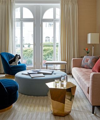 Living room with sofa and large circular ottoman and blue armchair and double french doors in the background.