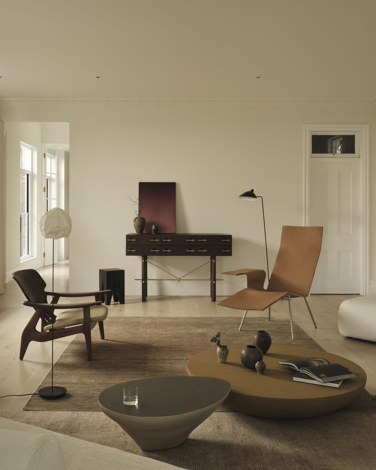 Image of a white living room with a dark console table on the back wall. There are two modern accent chairs facing each other and a pair of low nesting coffee tables in front of the chairs.