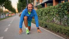 A smiling older man gets into the starting position as if he's going to run a foot race.