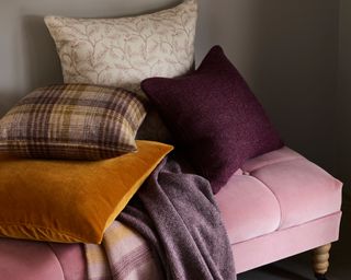 fall tone throw pillows and throw resting on a pink ottoman