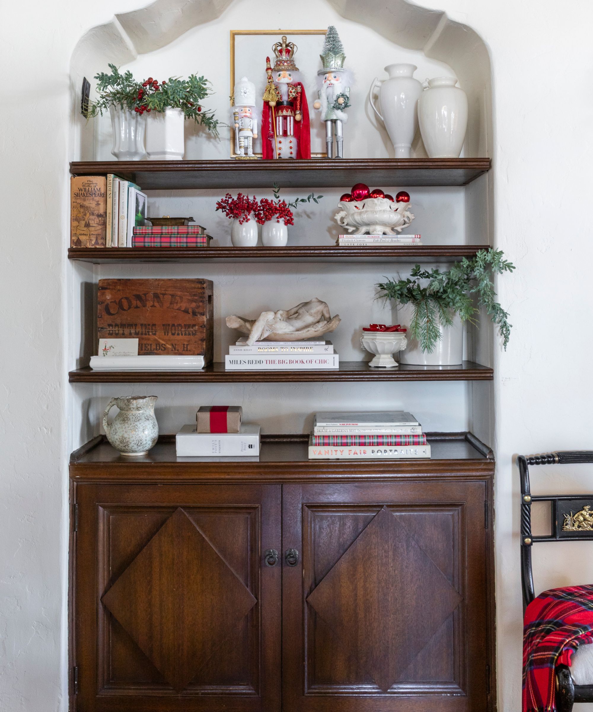 an alcove shelved niche with a dark wooden cupboard and shelves styled for christmas with nutcrackers and white china with red berries and green foliage