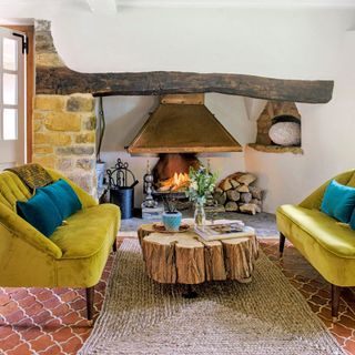 A cottage living room with yellow velvet sofas, natural tree trunk coffee table and fireplace