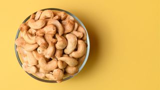Glass bowl of cashews on bright yellow background