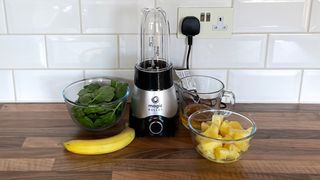 Nutribullet Magic Bullet Kitchen Express on a kitchen countertop surrounding by bowls of fruit and vegetables
