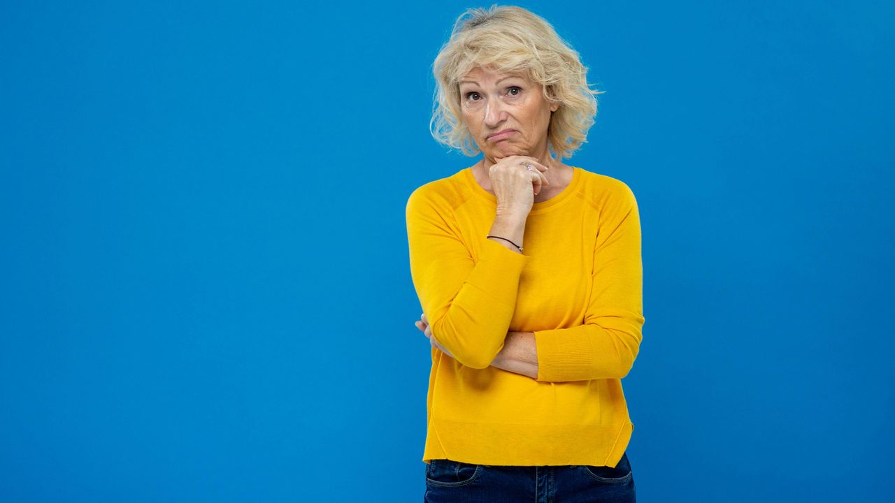 A woman with a dismayed look on her face stands with her chin resting on her hand.