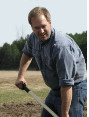 man wearing blue shirt and jeans digging a field