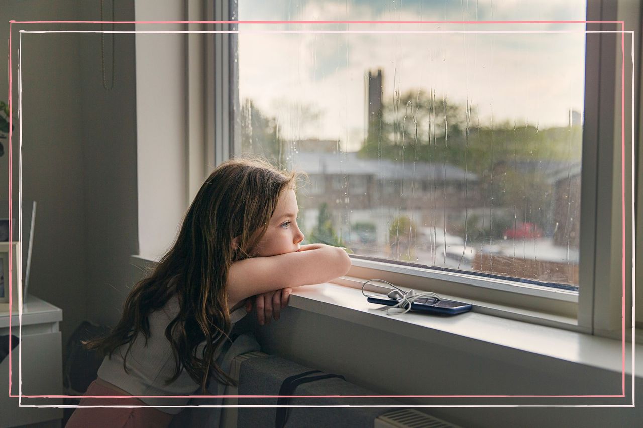 A young girl looking out of a window on a rainy day