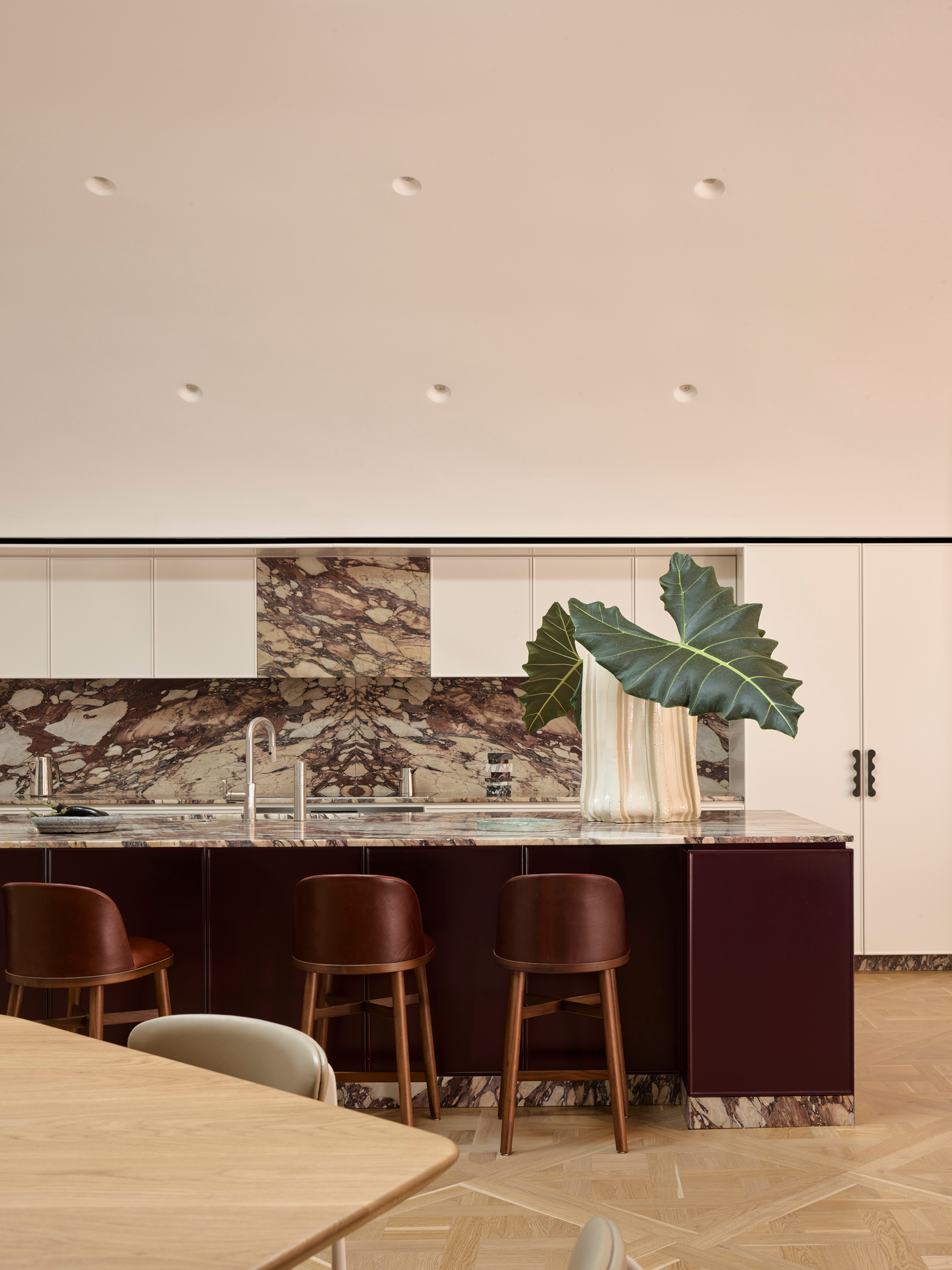 Kitchen with white wall units, burgundy island and marble backsplash and kickers