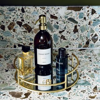 detail of a terrazzo bathroom countertop with a gold-framed mirror tray for toiletries