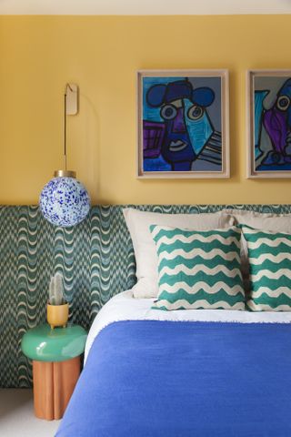 Yellow bedroom with green and blue wavy extended headboard, orange and green side table, cobalt blue throw and teal and white wavy throw pillows