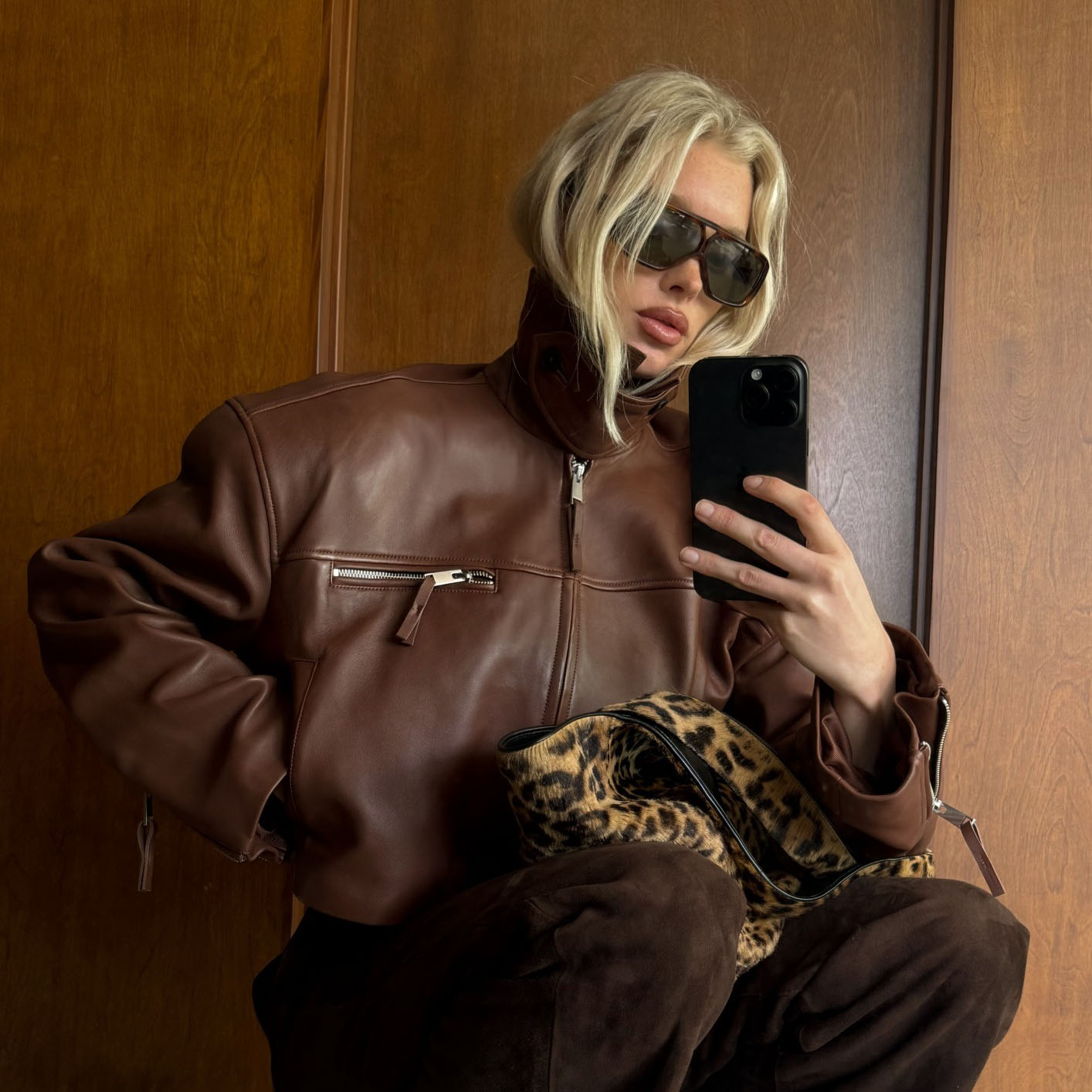 A woman wearing a brown leather jacket, cheetah print bag, and brown pants