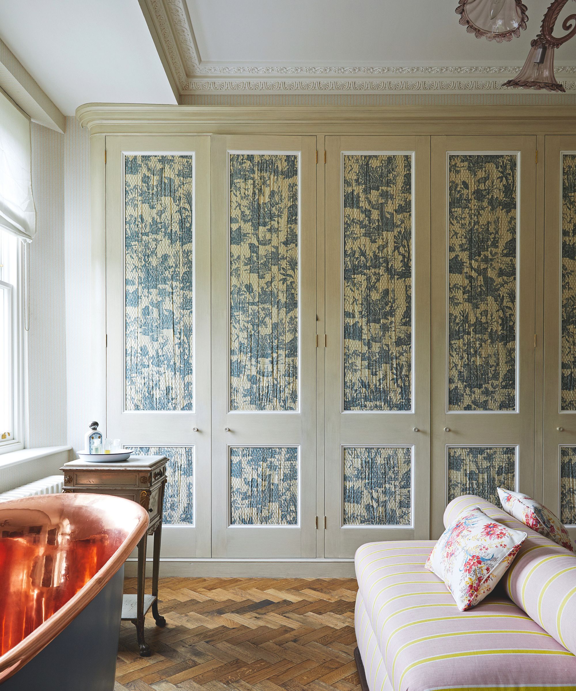neutral green bedroom with a copper freestanding bathtub and a row of taupe green wardrobes with tapestry print wallpapered door panels