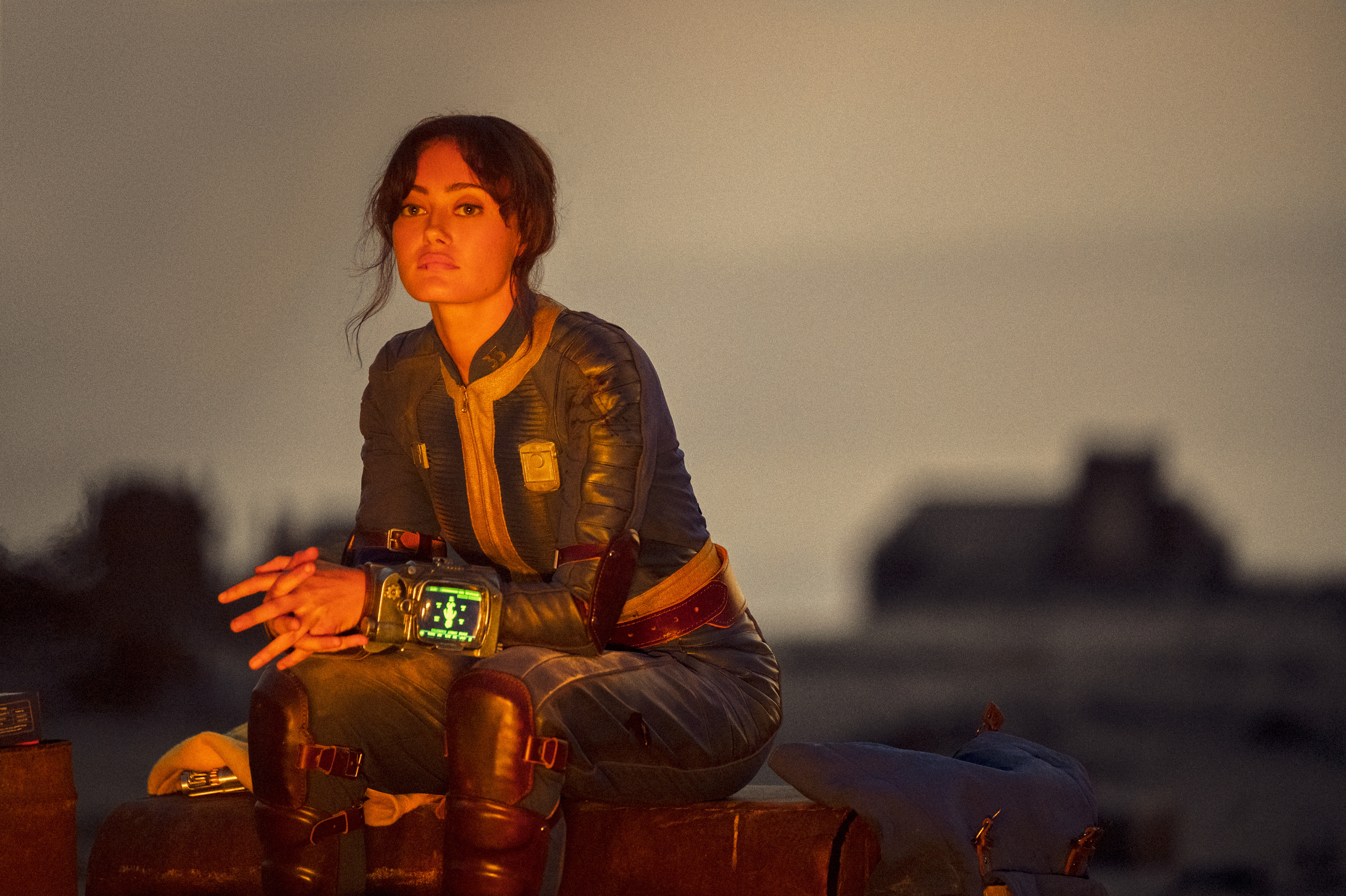 ella purnell as lucy maclean, sitting by a fire at dusk, in 'fallout'