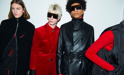 Models in font of a white wall in a row, black and red clothing with a couple wearing sunglasses