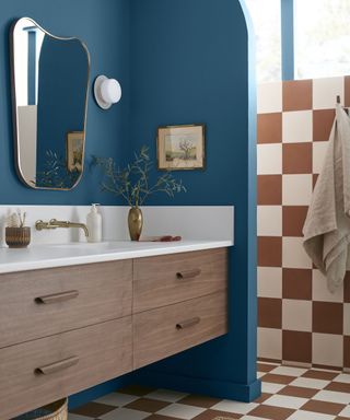 A bright bathroom with blue walls, orange and white checkered details, and a wooden and white marble vanity