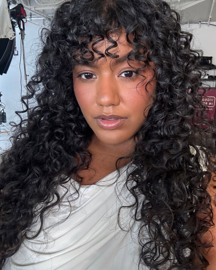A woman with long, curly hair and bangs.
