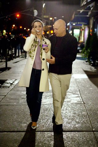 Kristin Davis as Charlotte York wearing a white coat, a scarf, a purple top, jeans, and heels