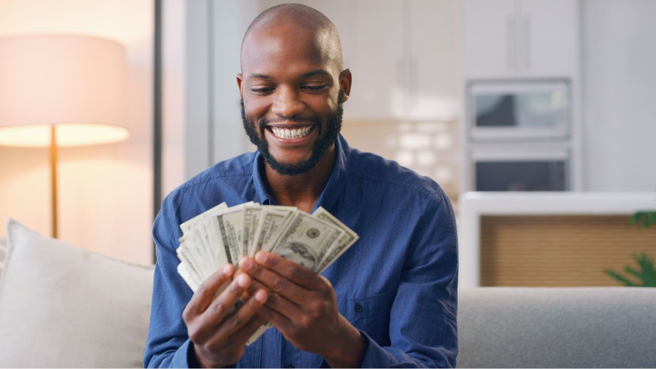 A man smiles as he looks at cash he&#039;s fanned out in his hands.