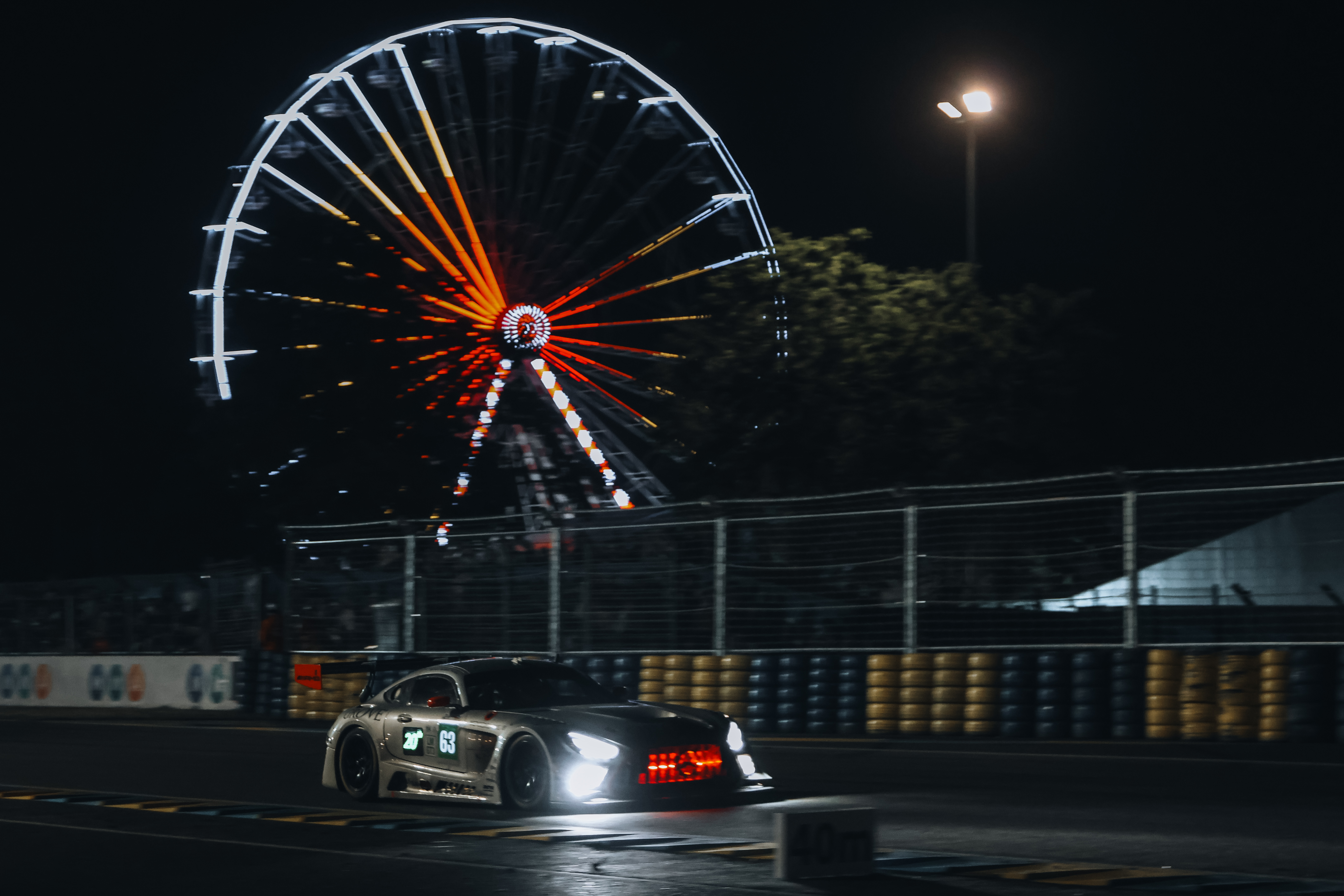 A car at Le Mans 2025 racing past a ferris wheel in the middle of the night