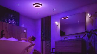 Philips Hue Xamento M lyser lilla i et badeværelse, hvor en kvinde ligger i boblebad