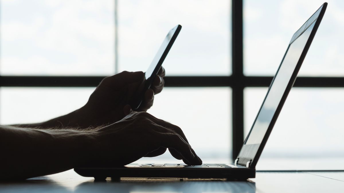 person working on laptop while on smartphone