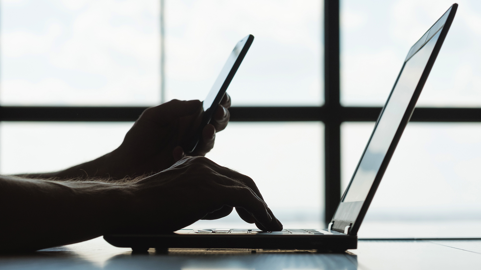 person working at laptop and looking at mobile phone