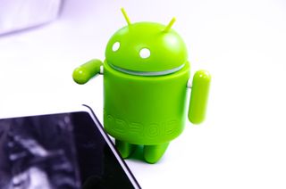 android robot standing next to a phone on a white desk