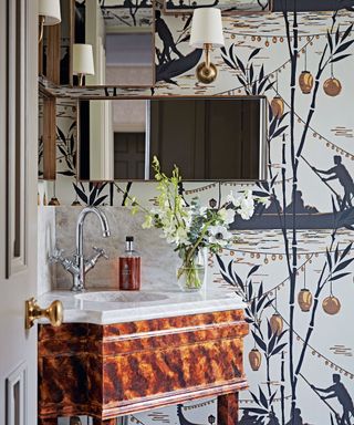View through doorway to wallpapered room with wooden vanity unit and grey marbled hand basin.
