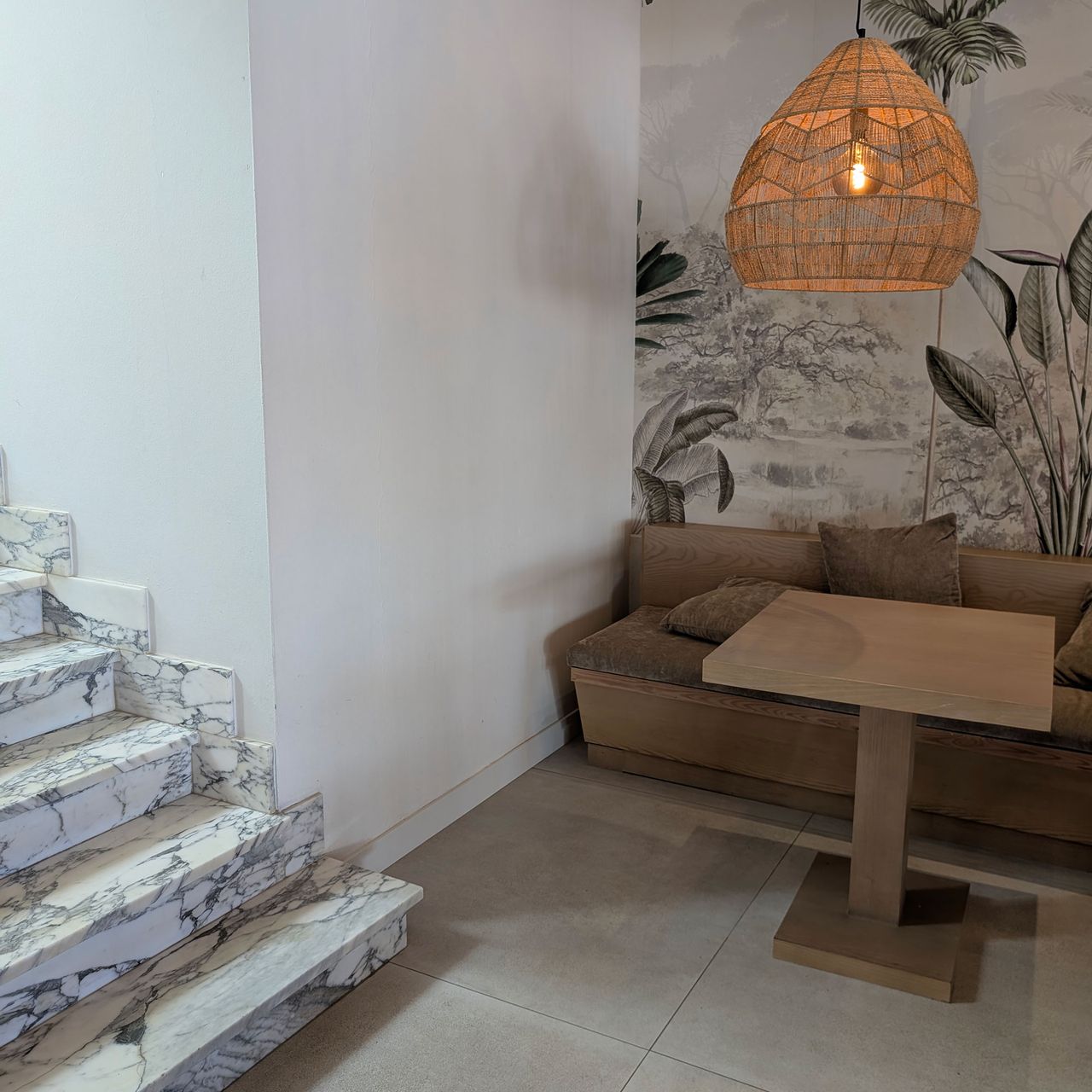 Large rattan lampshade above banquette seating with feature wall and beside marble staircase