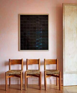 living room with pink wall, three wooden chairs and vinyl artwork