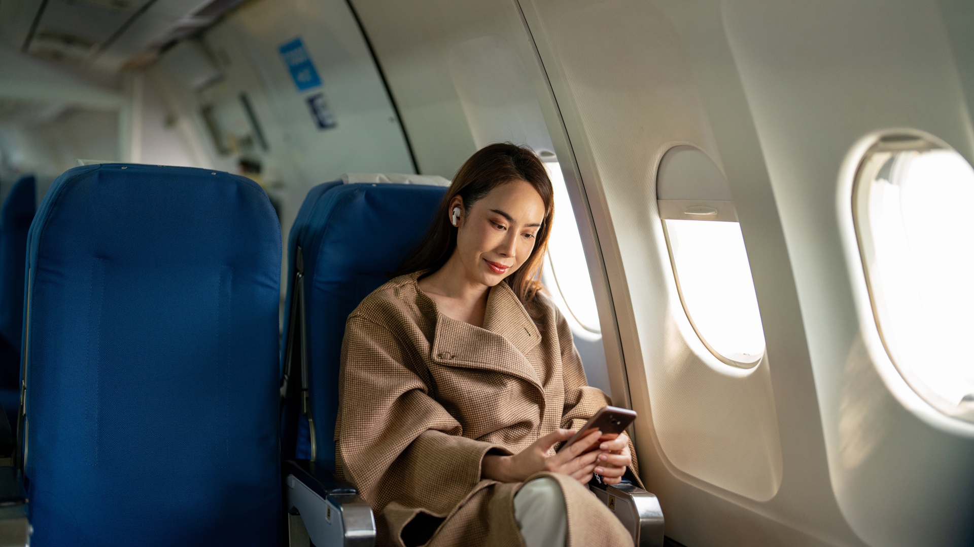 A focused businesswoman multitasking by using her phone while traveling on an airplane flight.