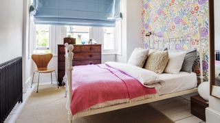 Bedroom with floral wallpaper, blue linen blinds, pink bedsheets and antique chest of drawers