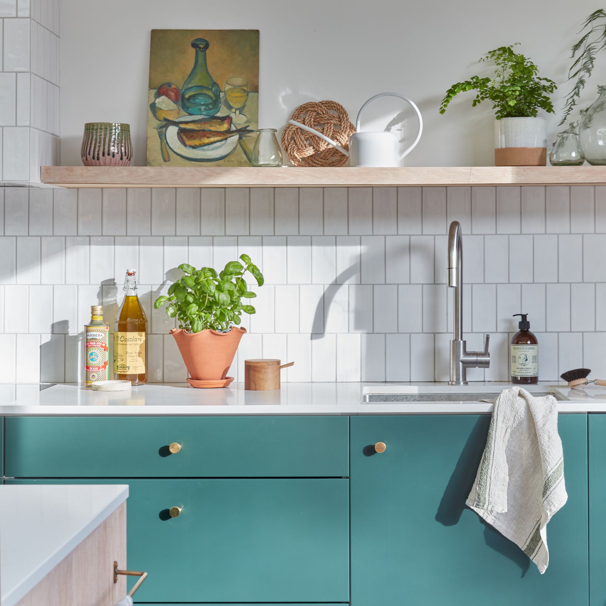 White tiled kitchen with teal cabinets and a shelf above the sink