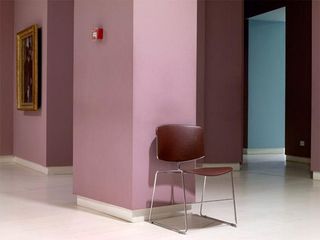 A lone hardwood chair is positioned with its back against a dusky-pink pillar in an art exhibition.