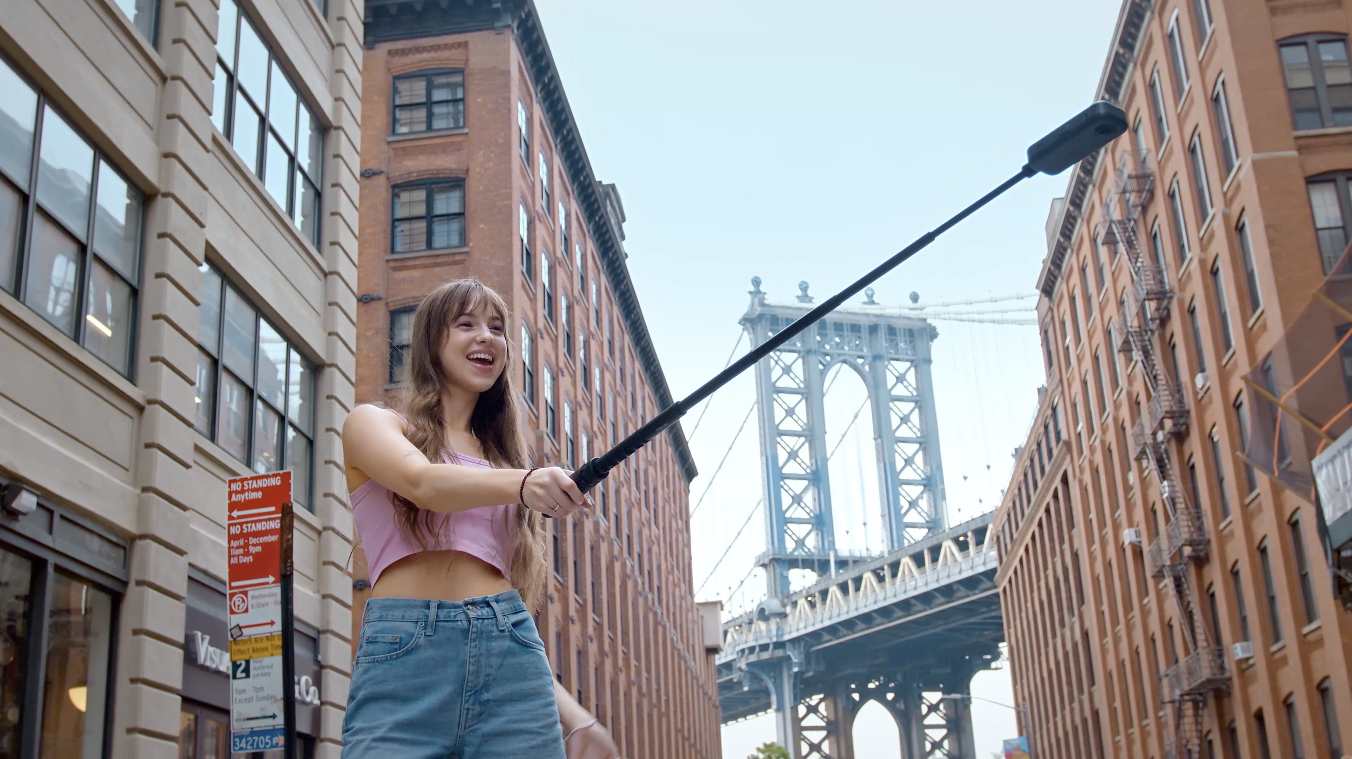 User holding a long selfie stick with Akaso 360 camera attached, Brooklyn bridge backdrop