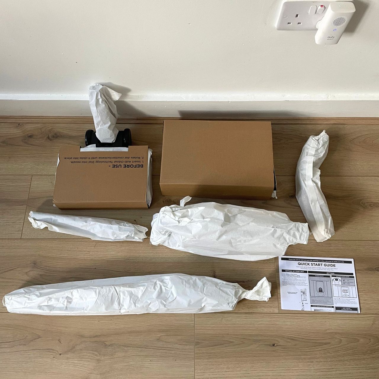 Shark Stratos Cordless Vacuum components wrapped in paper, laying out on a wood-effect flooring