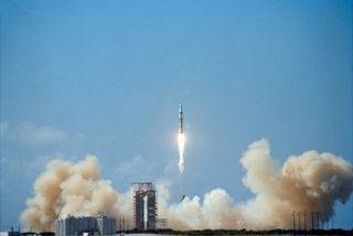 a white rocket lifts off above a cloud of smoke under blue skies