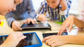Four kids work on three touch screen tablet computers