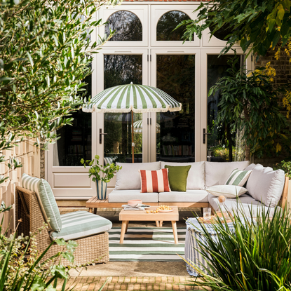 Habitat green striped Sunbeam parasol on a patio. There is a green striped garden accent chair, grey sofa set and wood coffee table.