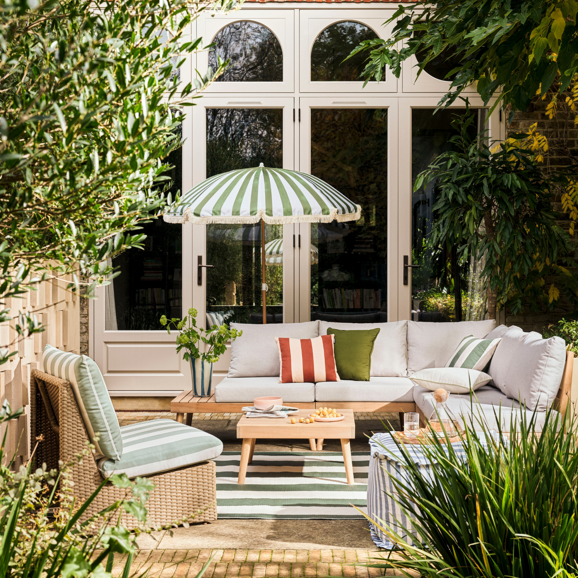 Habitat green striped Sunbeam parasol on a patio. There is a green striped garden accent chair, grey sofa set and wood coffee table.