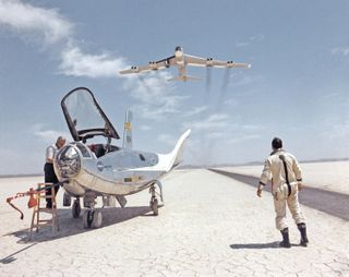 After a research flight by the HL-10 lifting body, technician John Reeves works on the craft, and pilot Bill Dana watches the B-52 that launched it.