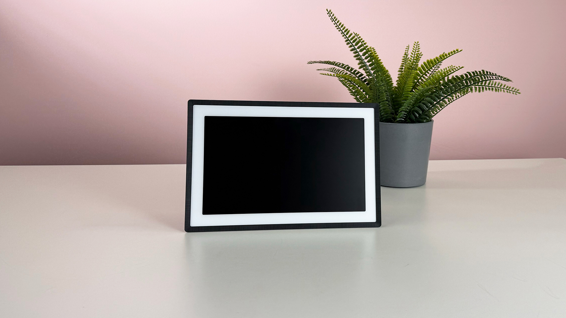 The Pexar 11-inch Digital Picture Frame in horizontal orientation in front of a pot plant and a pink background.