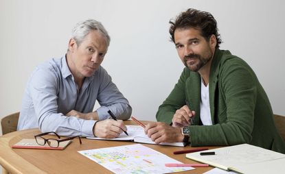 Designers Jasper Morrison and Jaime Hayon sitting at a desk with papers all over it.