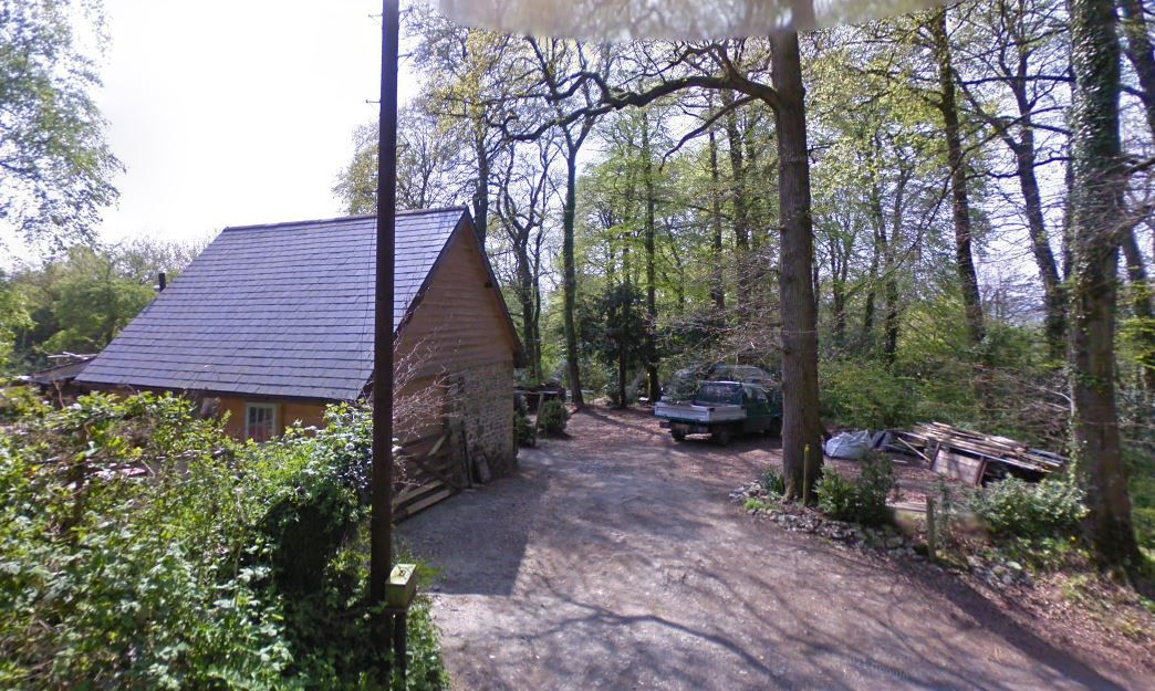 The proposed site showing a small wooden barn with dirt track and cars around it