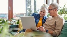 White older straight couple sitting on the couch, smiling looking at a laptop together