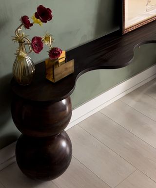 A green-painted hallway with a wavy dark-wood console table with sphere-shaped legs made using IKEA serving bowls